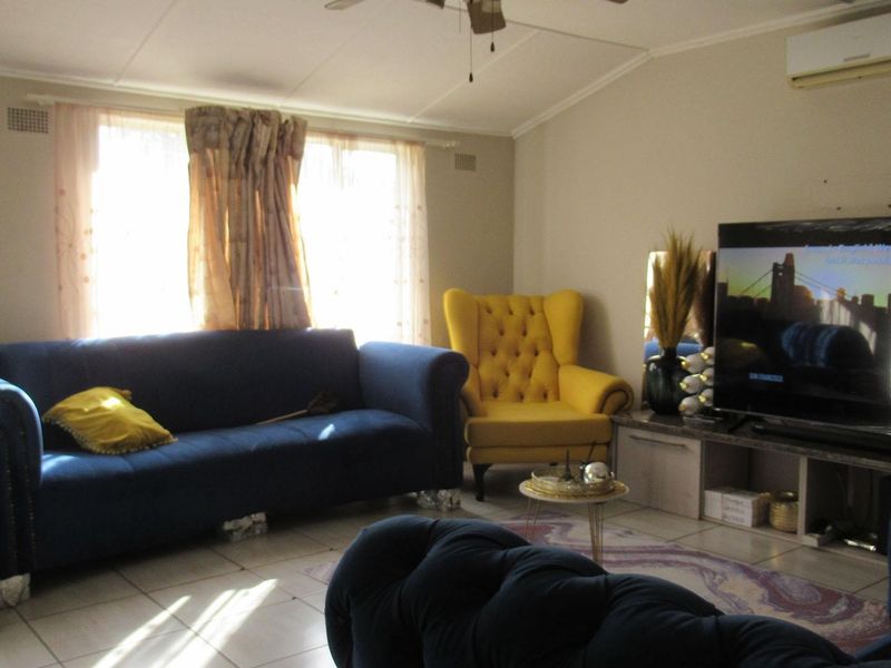 A comfortable living room featuring tiled flooring, a ceiling fan, and a wall-mounted split-system air conditioner for climate control.