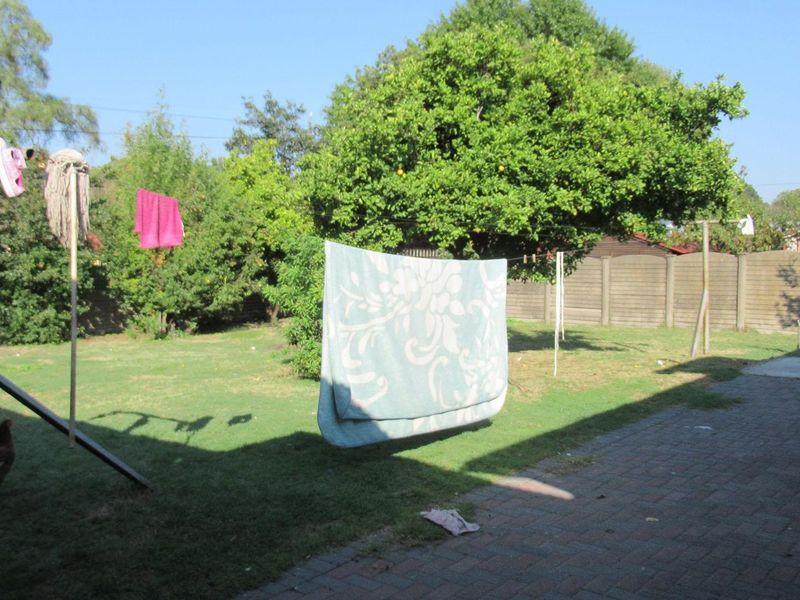 A spacious backyard featuring a lawn, mature trees, a paved patio area, and a precast concrete boundary wall.