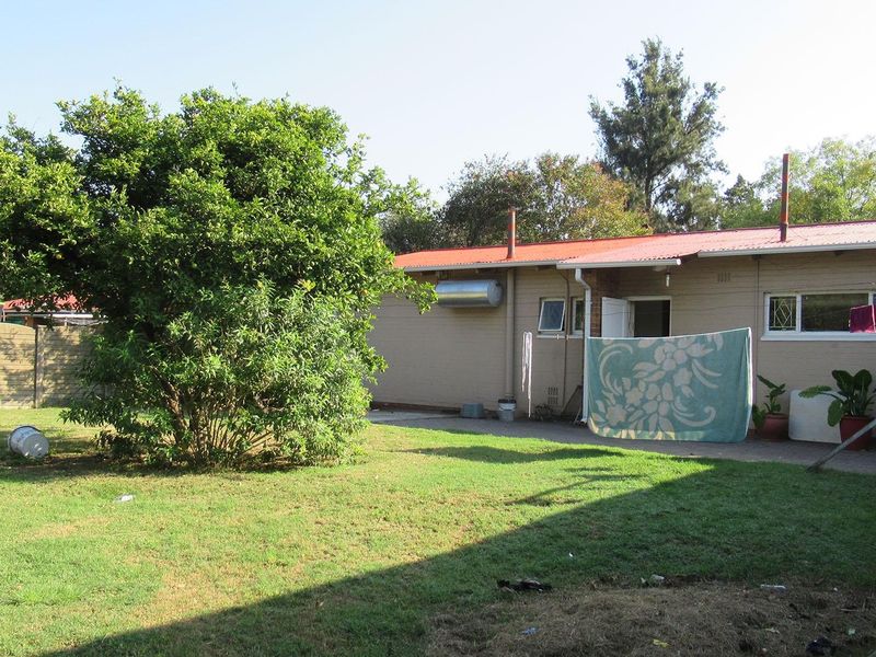 Rear view of the property featuring a brick facade, corrugated metal roof, solar water heater, and a paved patio area overlooking the garden.