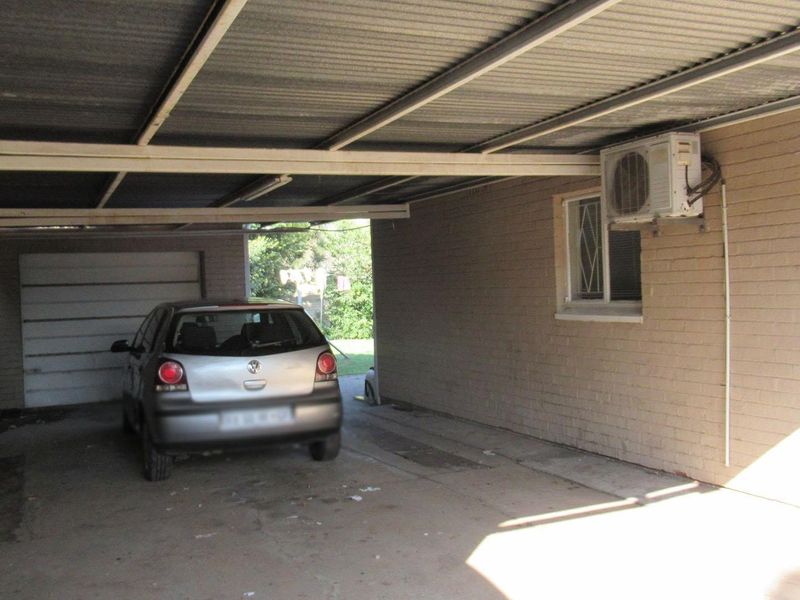A covered carport or garage area featuring brick walls, a corrugated metal roof, and a mounted air conditioning unit.