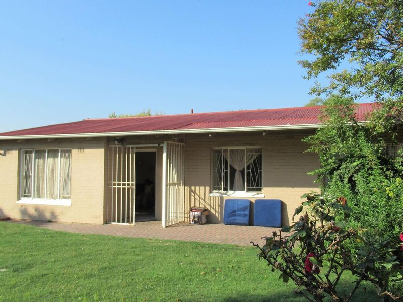 Rear view of a single-story brick house featuring a corrugated metal roof, paved patio area, and security-fitted windows and doors.