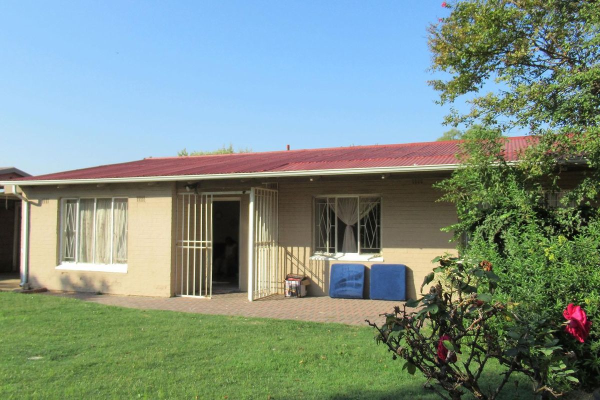 Rear view of a single-story brick house featuring a corrugated metal roof, paved patio area, and security-fitted windows and doors.