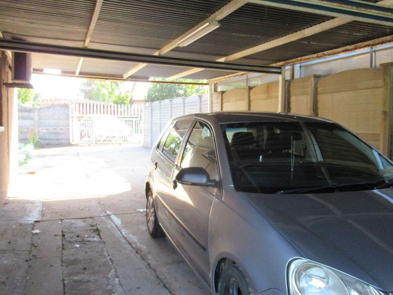 A covered carport area featuring a corrugated metal roof, precast concrete boundary walls, and a concrete driveway.
