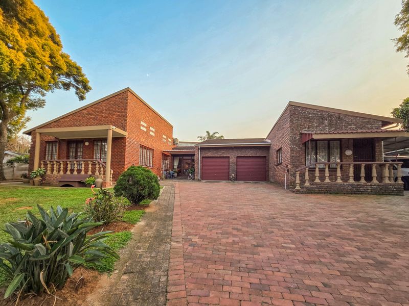 Front view of a brick house featuring a double garage, paved driveway, and covered porches with decorative balustrades.