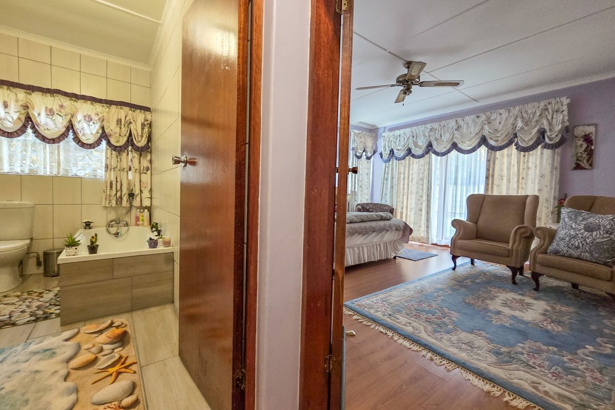 A bedroom featuring laminate flooring and a ceiling fan, with an adjoining en-suite bathroom equipped with a built-in bathtub and tiled walls.