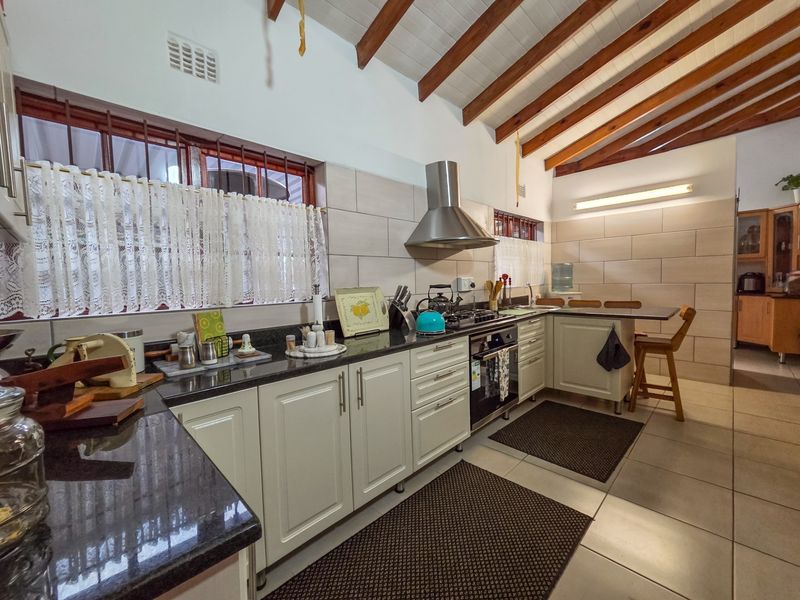 A well-maintained kitchen featuring granite countertops, built-in cabinetry, stainless steel extractor fan, and exposed timber ceiling beams, offering a functional and classic aesthetic.