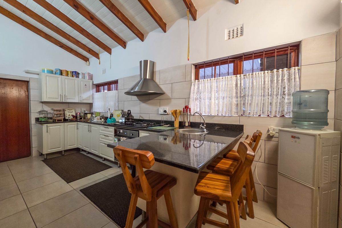 A functional kitchen featuring granite countertops, a gas hob, stainless steel extractor fan, and exposed timber ceiling beams, offering a warm and practical workspace.