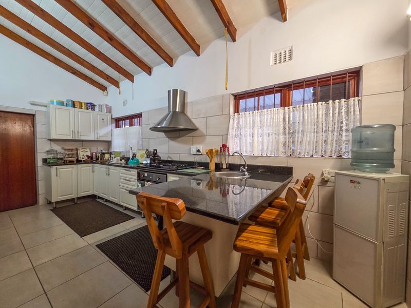 A functional kitchen featuring granite countertops, a gas hob, stainless steel extractor fan, and exposed timber ceiling beams, offering a warm and practical workspace.