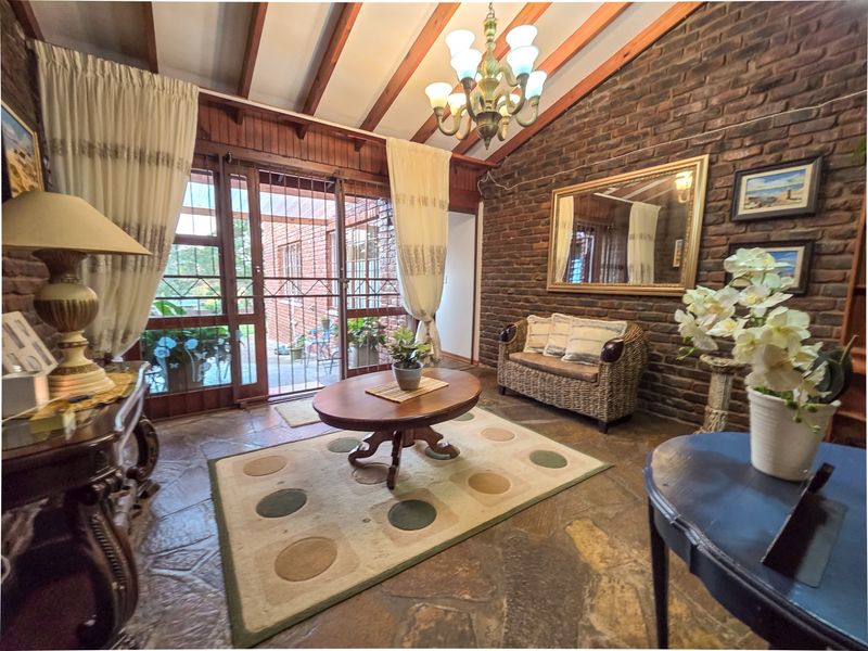 A rustic living room featuring exposed brick walls, flagstone flooring, and timber ceiling beams, with large sliding doors providing access to the outdoor area.