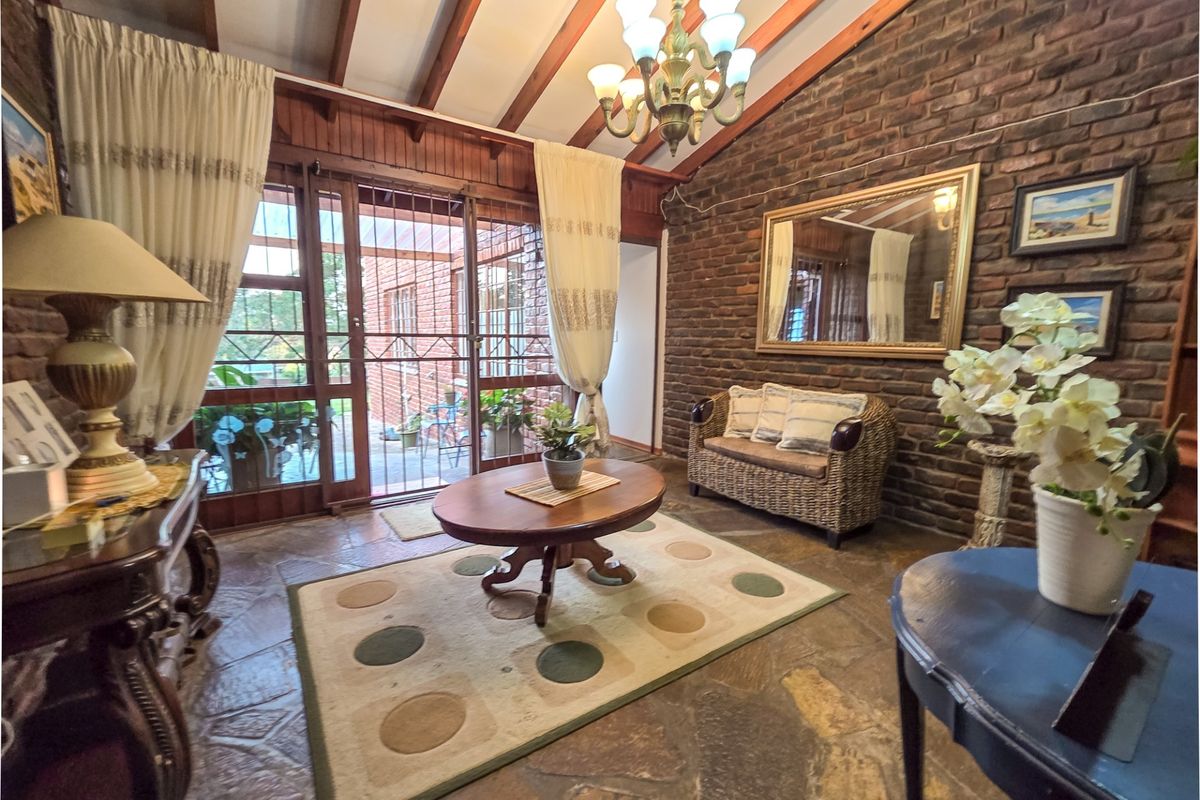 A rustic living room featuring exposed brick walls, flagstone flooring, and timber ceiling beams, with large sliding doors providing access to the outdoor area.