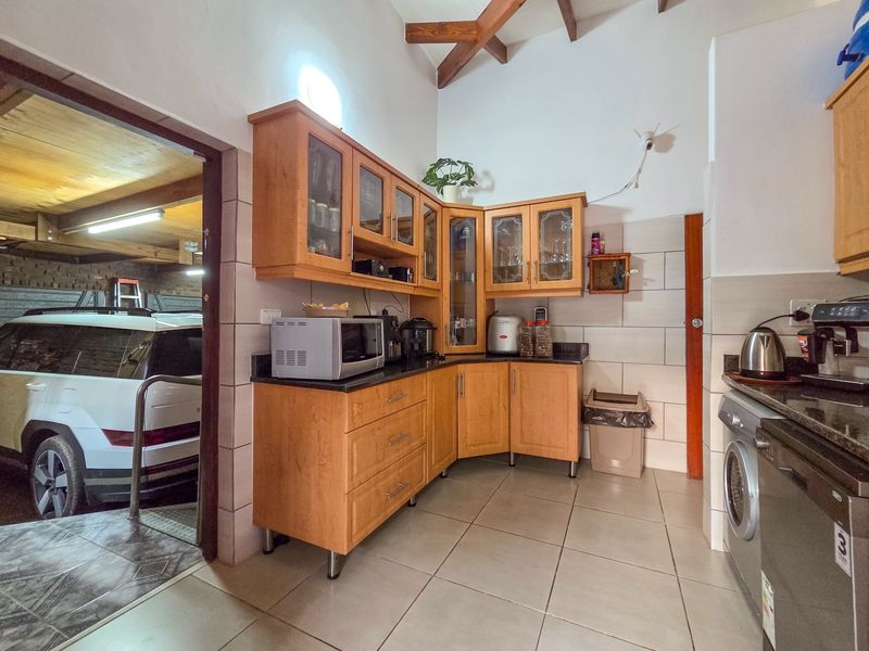 A functional kitchen featuring wooden cabinetry, granite countertops, tiled flooring, and exposed timber ceiling beams, with direct access to the garage area.