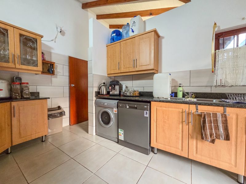 Functional kitchen featuring wooden cabinetry, granite countertops, tiled backsplash, and integrated laundry and dishwasher appliances under exposed ceiling beams.