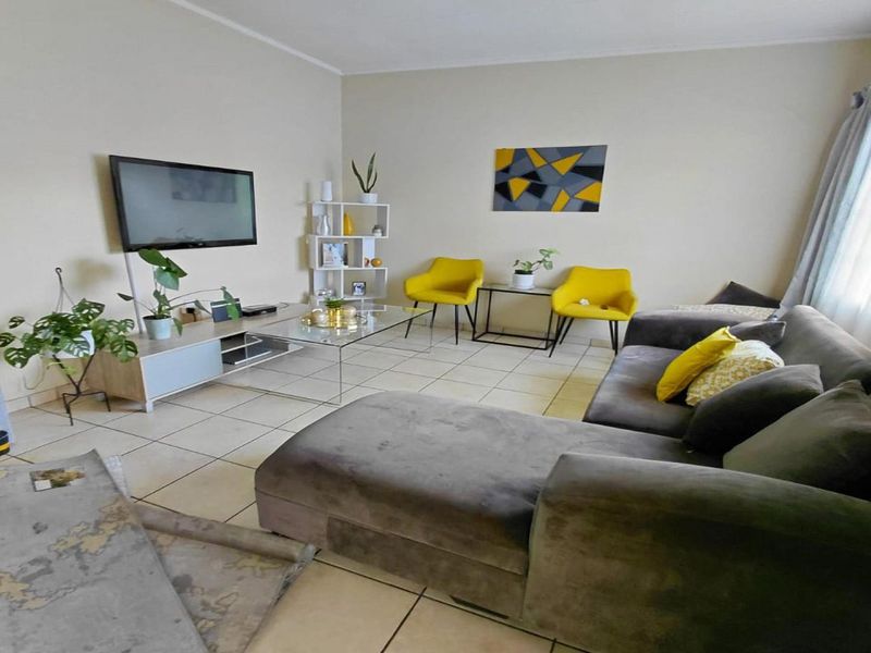 A comfortable living room featuring neutral tiled flooring and large windows with curtain rails, providing a bright and functional space for relaxation.