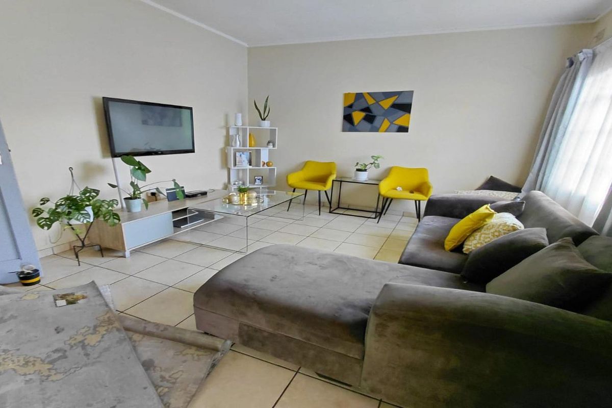 A comfortable living room featuring neutral tiled flooring and large windows with curtain rails, providing a bright and functional space for relaxation.