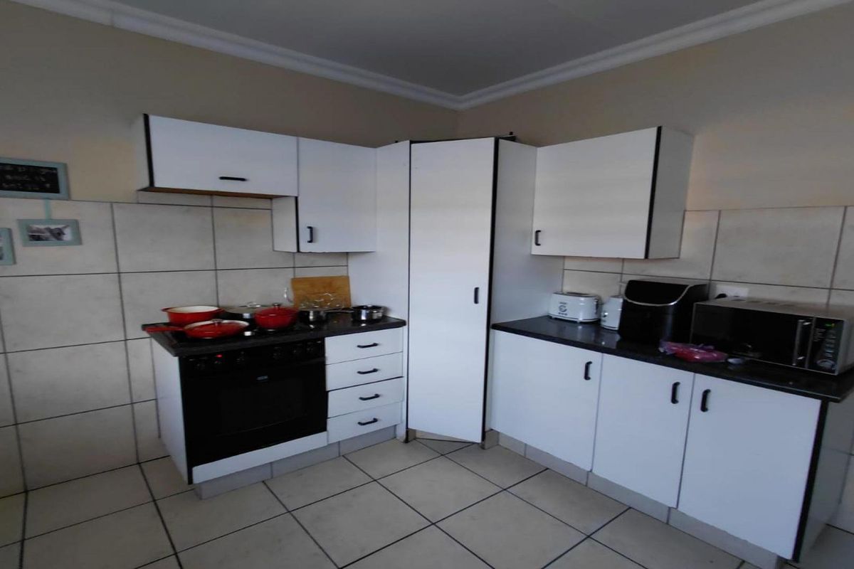 A functional kitchen featuring white built-in cabinetry, dark laminate countertops, a built-in oven and hob, and tiled flooring with a tiled splashback.