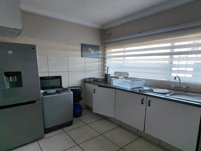 A functional laundry area featuring built-in cabinetry, a stainless steel sink, tiled splashbacks, and tiled flooring with natural light from a large window.