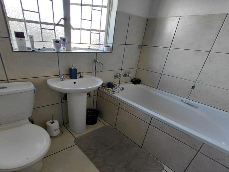 A functional bathroom featuring a pedestal basin, toilet, and bathtub with tiled finishes and a window with security bars.