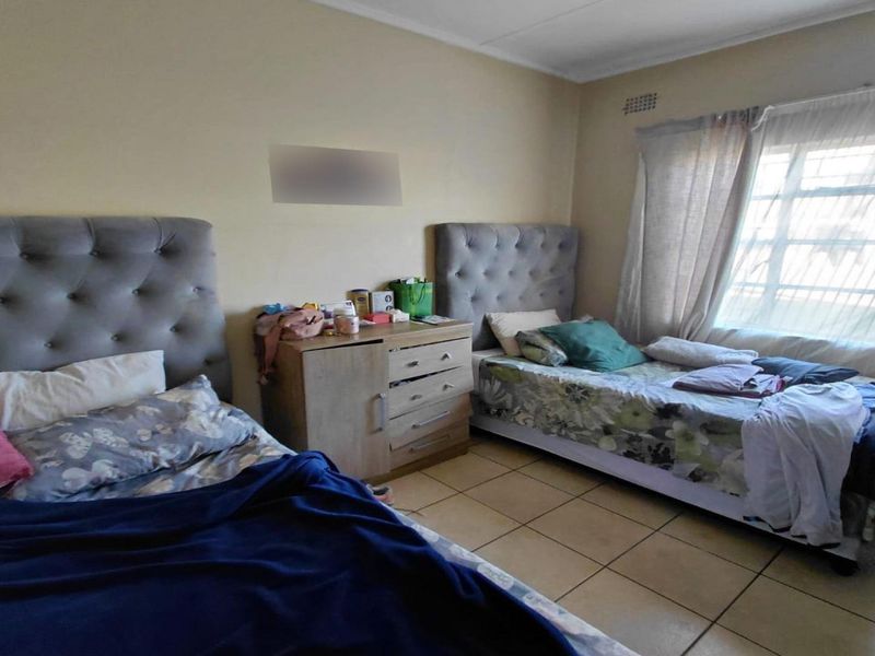 A functional bedroom featuring tiled flooring and a window fitted with security burglar bars.