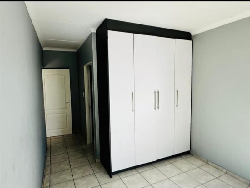 A clean, empty bedroom featuring neutral grey walls, tiled flooring, and a modern built-in wardrobe with white and black finishes.