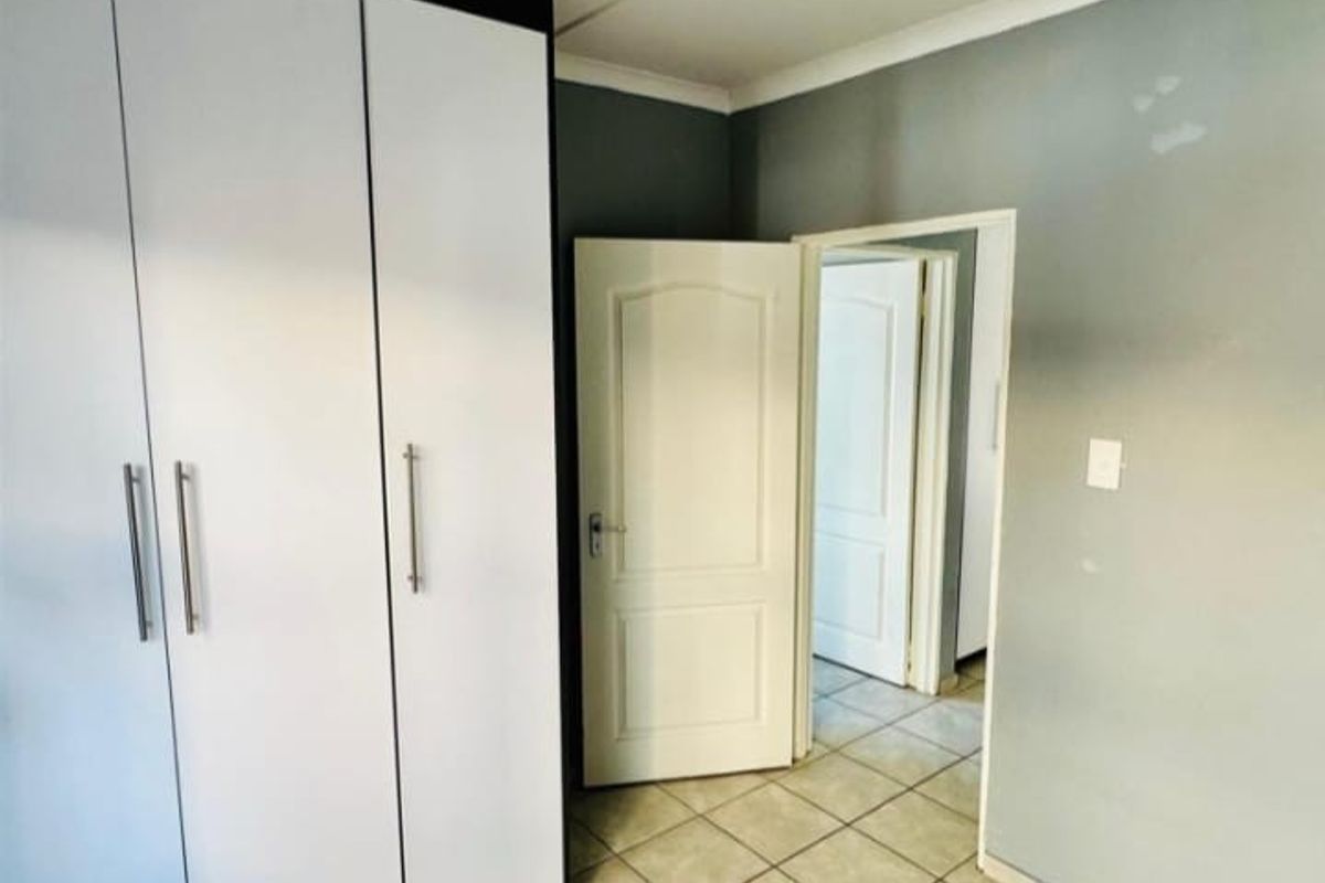 A bedroom featuring built-in cupboards, tiled flooring, and neutral wall finishes, providing a clean and functional space ready for personalization.