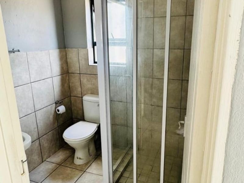 A compact bathroom featuring a shower enclosure, toilet, and neutral tiled finishes, requiring some ceiling maintenance and cosmetic updates.