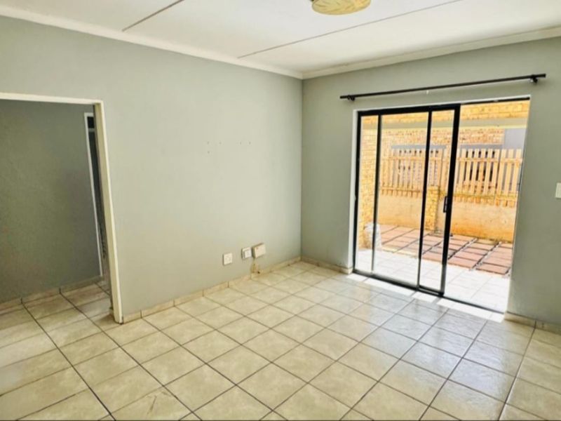 An empty living room featuring tiled flooring and a sliding glass door providing access to an outdoor patio area.