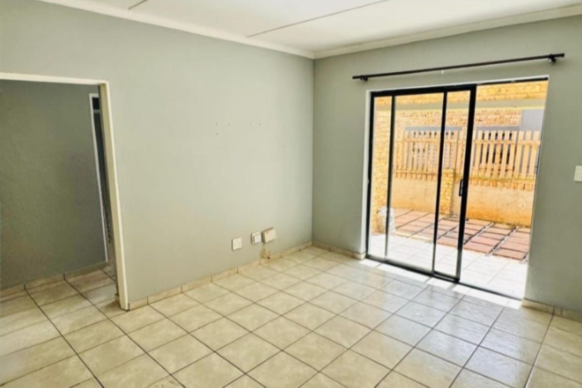 An empty living room featuring tiled flooring and a sliding glass door providing access to an outdoor patio area.