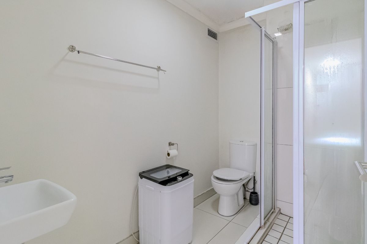 A functional bathroom featuring a wall-mounted basin, a toilet, and a glass-enclosed shower with tiled flooring.