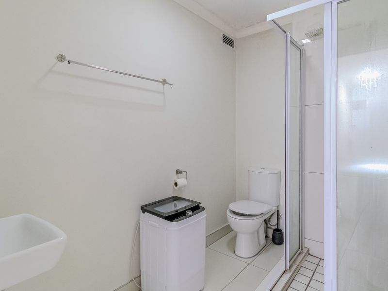 A functional bathroom featuring a wall-mounted basin, a toilet, and a glass-enclosed shower with tiled flooring.