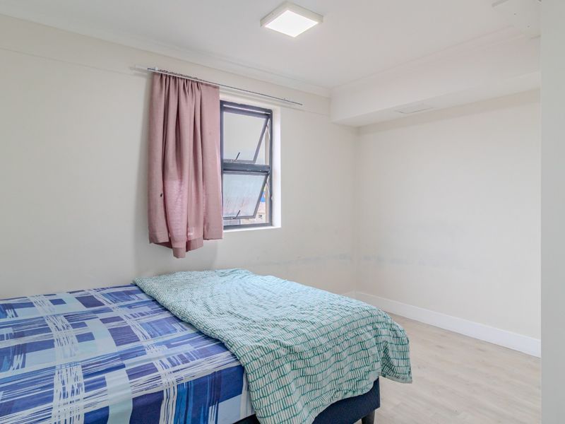 A simple bedroom featuring light-toned laminate flooring, a top-hung window, and neutral wall finishes.