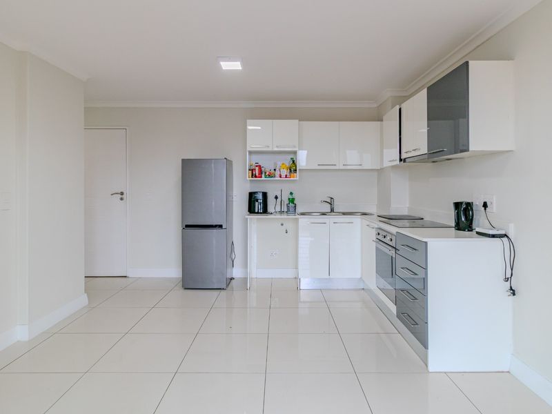 Modern kitchen featuring white and grey cabinetry, integrated appliances, and clean tiled flooring in an open-plan layout.