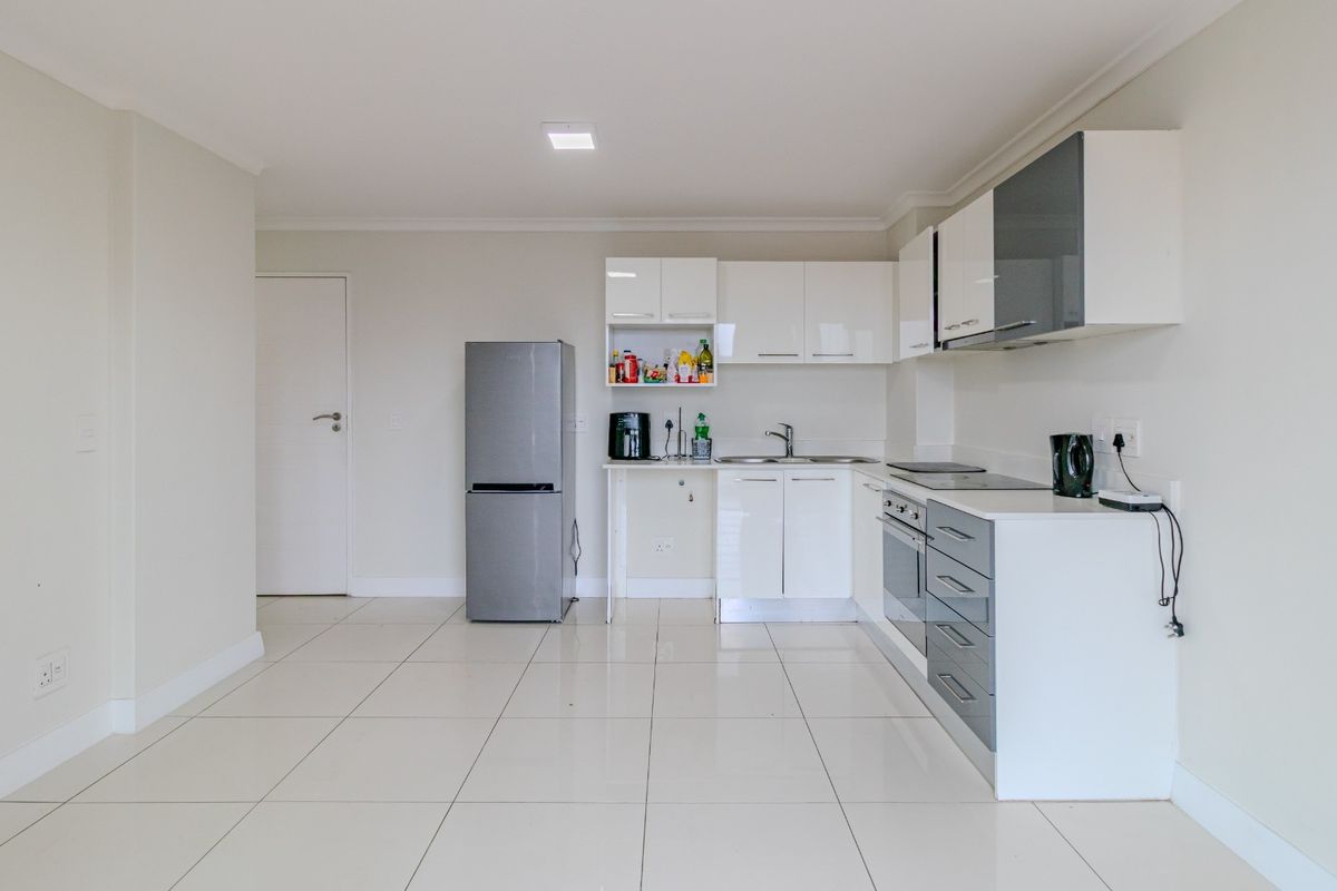 Modern kitchen featuring white and grey cabinetry, integrated appliances, and clean tiled flooring in an open-plan layout.