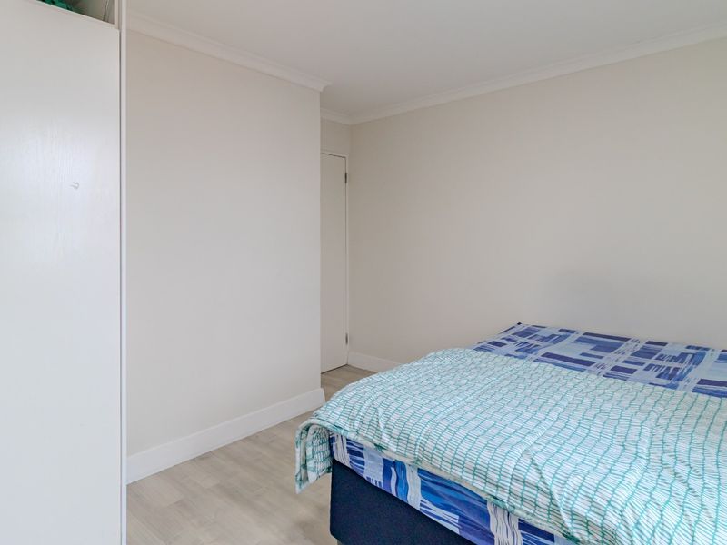 A clean bedroom featuring light laminate flooring, neutral walls, and a built-in wardrobe, offering a simple and functional living space.
