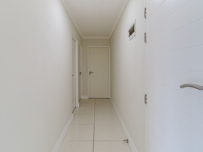 A clean, well-maintained hallway featuring white tiled flooring and multiple internal doors, providing access to various rooms within the apartment.