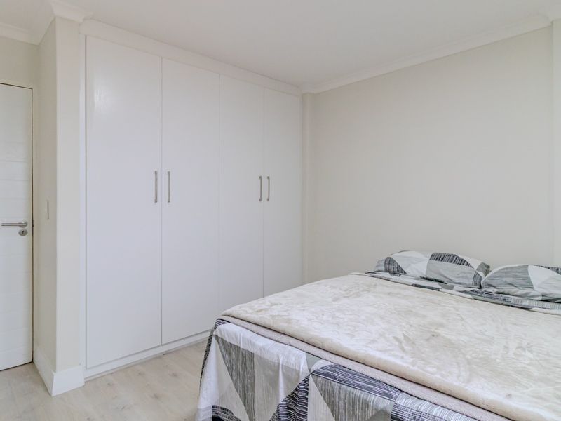 A clean and well-maintained bedroom featuring neutral walls, light-toned flooring, and ample built-in cupboard storage.