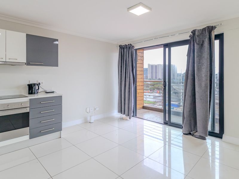 Modern open-plan kitchen and living area featuring sleek cabinetry, built-in appliances, tiled floors, and direct access to a balcony with city views.