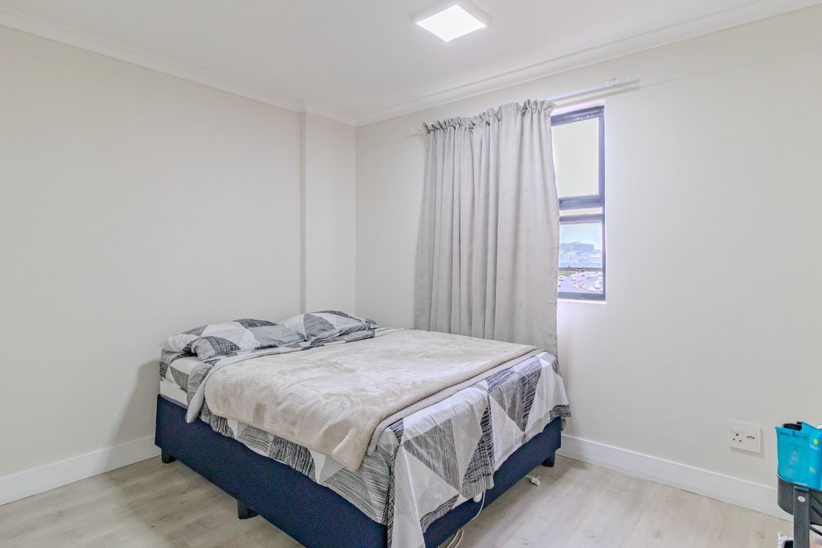 A clean and neutral bedroom featuring light laminate flooring, coving, and a window with natural light.