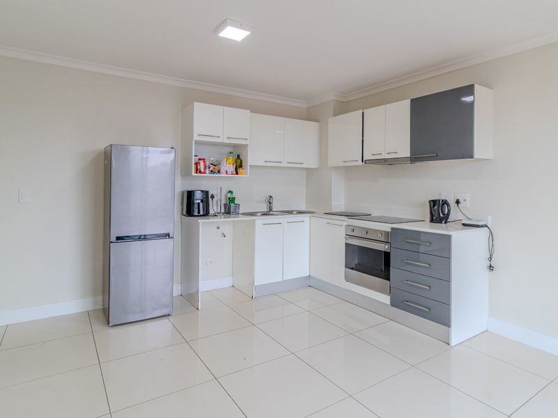 Modern kitchen featuring white and grey cabinetry, integrated oven and hob, stainless steel sink, and clean tiled flooring.