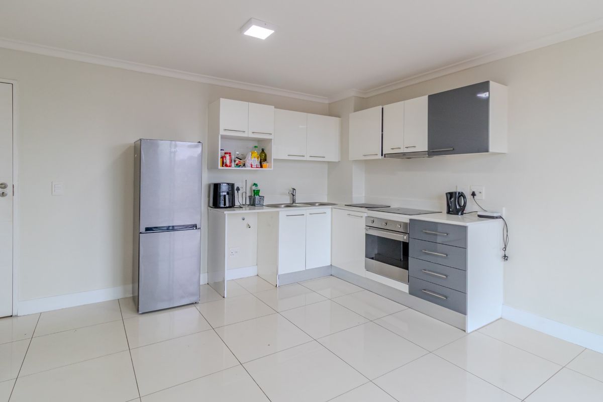 Modern kitchen featuring white and grey cabinetry, integrated oven and hob, stainless steel sink, and clean tiled flooring.