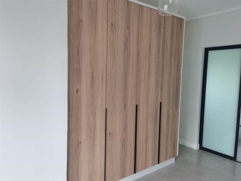 A modern bedroom featuring sleek, wood-grain built-in wardrobes with black handles and neutral tiled flooring.