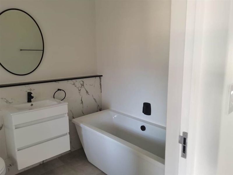 Modern bathroom featuring a sleek freestanding bathtub, wall-mounted vanity, and contemporary black matte fixtures against elegant marble-look wall tiling.