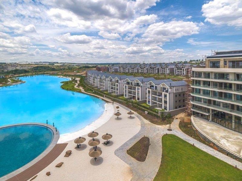 Aerial view of a modern apartment complex featuring a large swimming pool, landscaped grounds, and contemporary residential architecture.