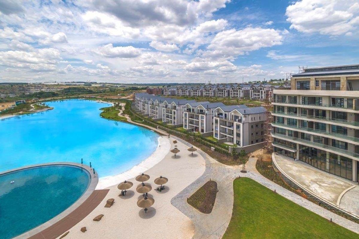 Aerial view of a modern apartment complex featuring a large swimming pool, landscaped grounds, and contemporary residential architecture.