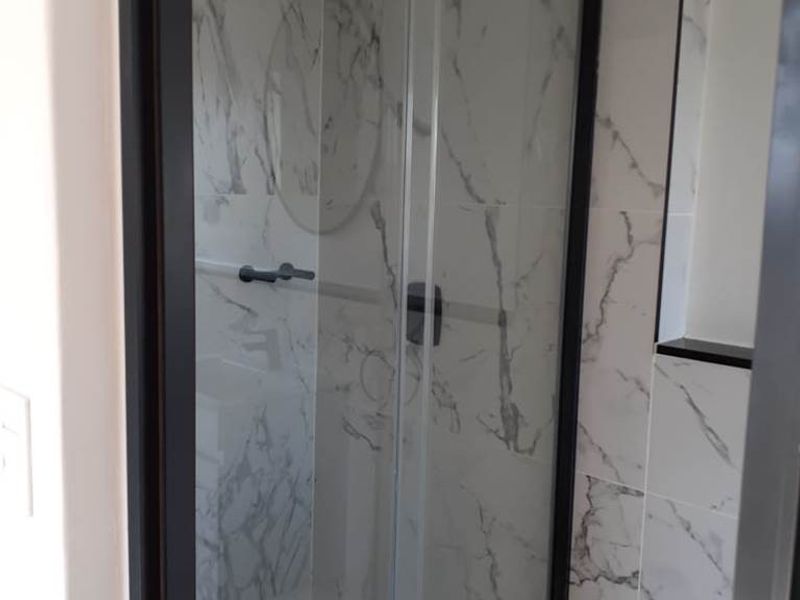 Modern bathroom featuring a sleek glass shower enclosure with black framing and elegant marble-look wall tiles.