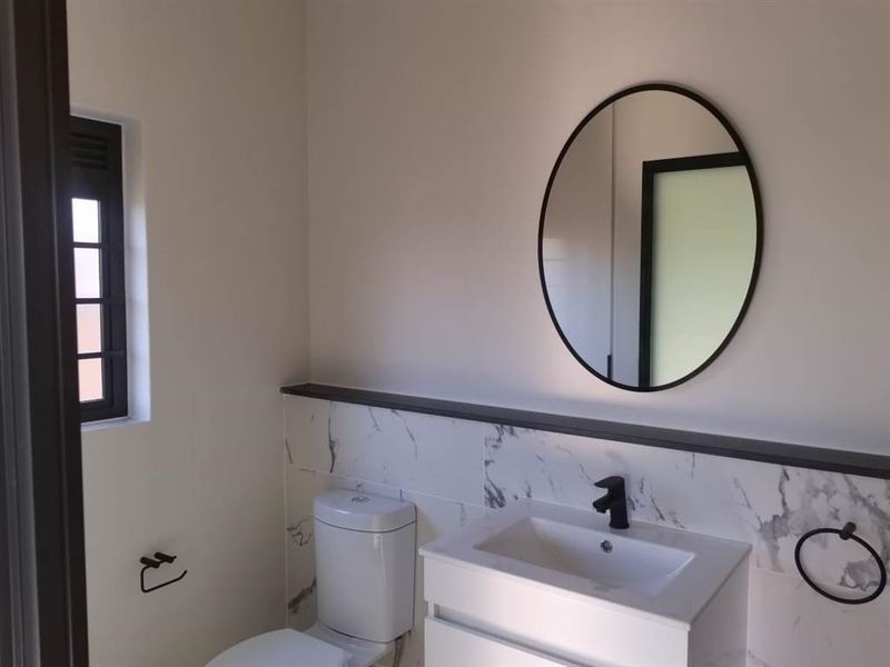 A modern, clean bathroom featuring a vanity with a basin, black mixer tap, round mirror, and marble-look wall tiling.