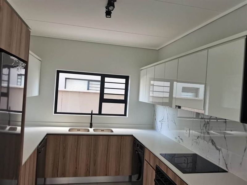 Modern kitchen featuring sleek white and wood-grain cabinetry, stone countertops, marble-look splashback, and integrated appliances including a hob and oven.