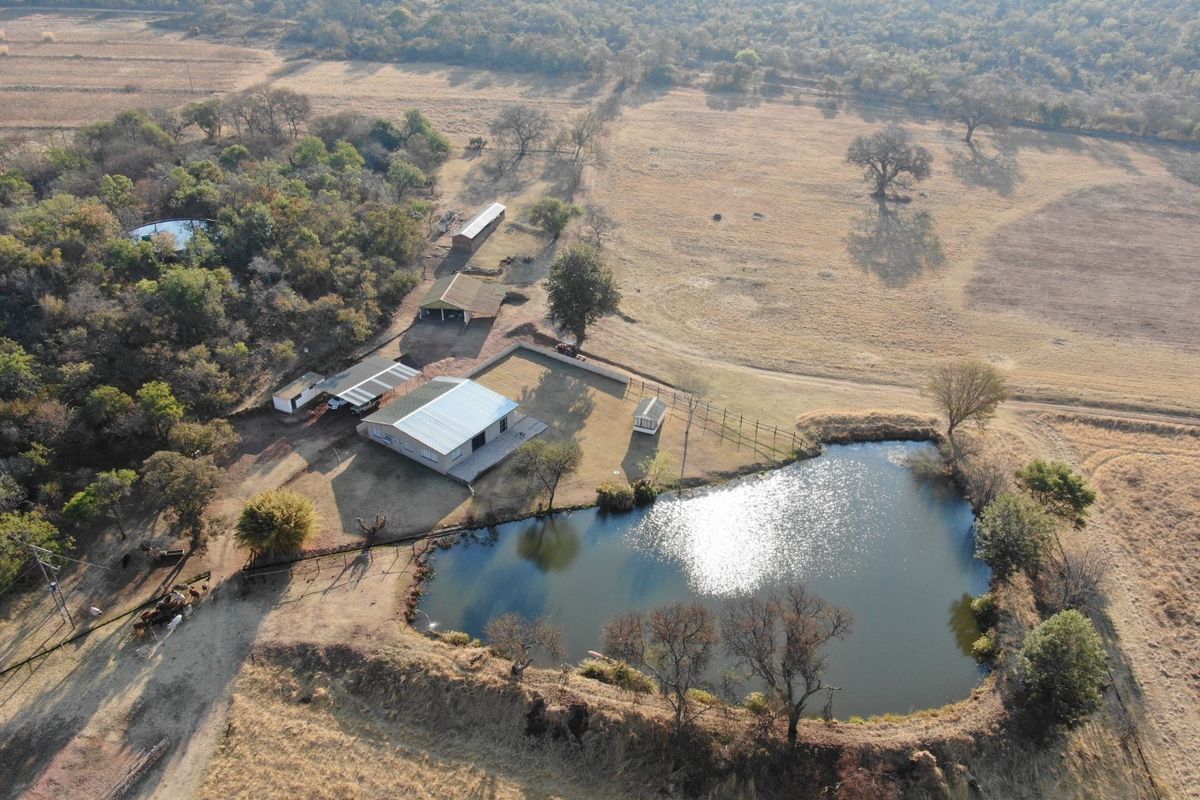 Aerial view of a farm property featuring a large dam, main dwelling with a metal roof, and various outbuildings set within open grazing land.