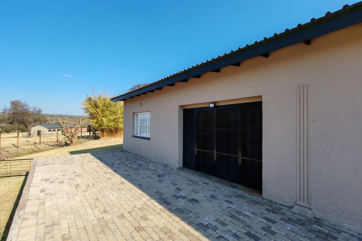 Rear exterior view of the farm building featuring a paved patio area, metal security gate, and corrugated roof structure.