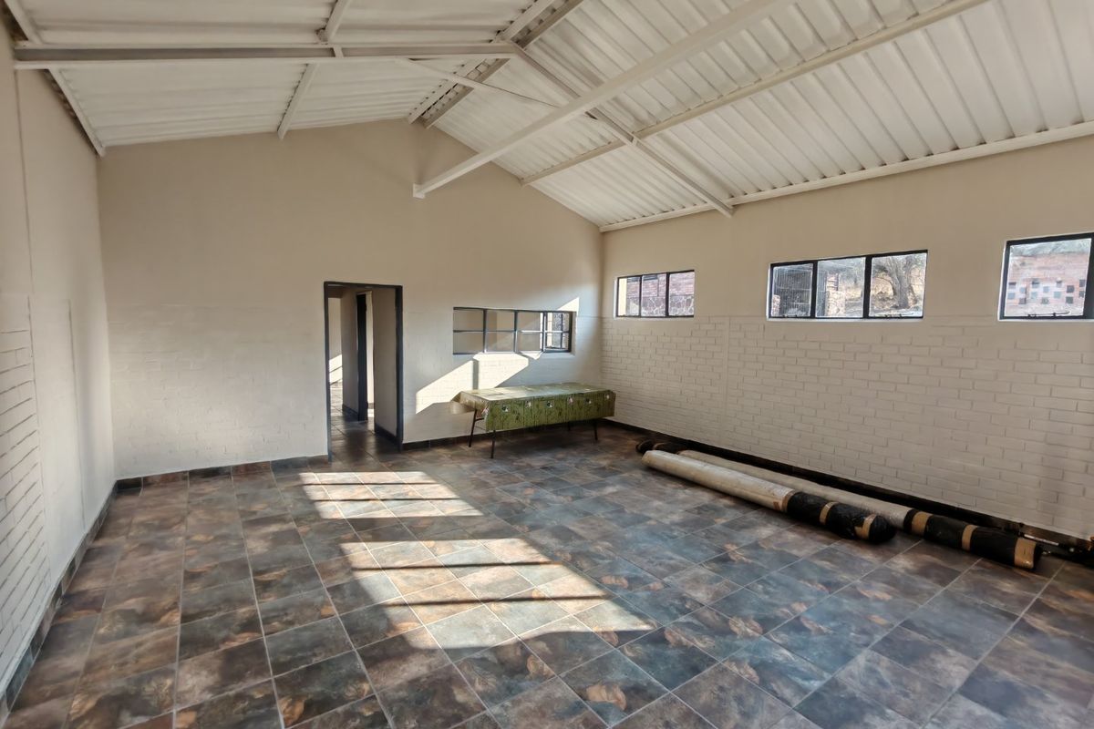 A spacious, empty living area featuring exposed beam ceilings, tiled flooring, and painted brick walls, offering a versatile blank canvas for interior design.