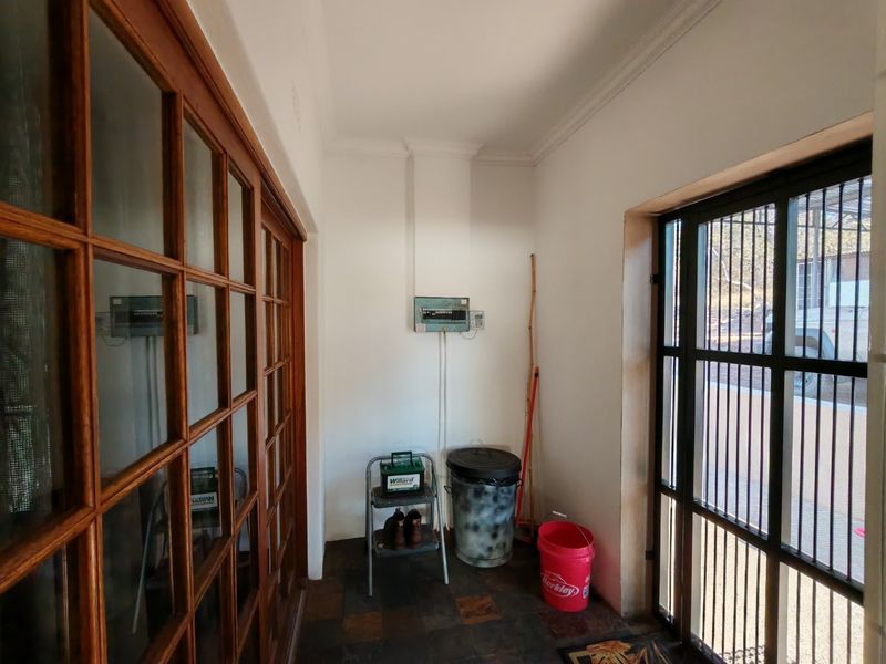 A functional utility space featuring slate tile flooring, an electrical distribution board, and secure access via timber-framed glass doors and a security gate.